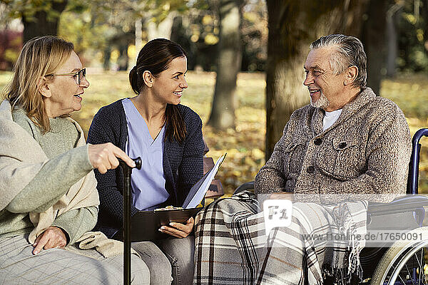 Smiling nurse discussing documents with senior couple at park