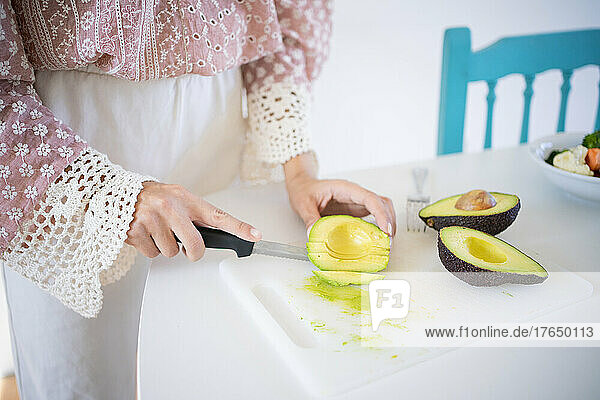 Young woman chopping avocado standing at table