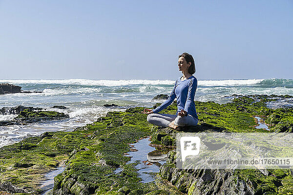 Woman sitting in lotus position and meditating on rock at beach