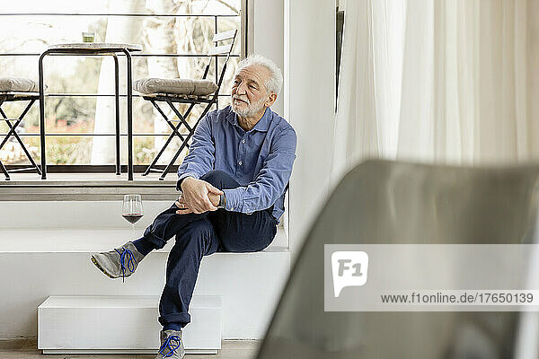 Senior man sitting with legs crossed at knee in front of window at home