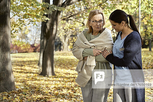 Senior woman talking with nurse walking at public park