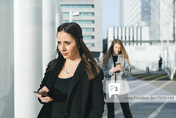 Young woman holding smart phone standing in front of friend