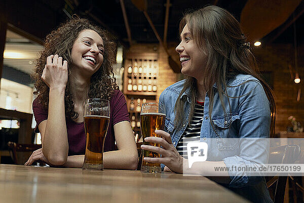 Zwei glückliche Freundinnen trinken Bier und unterhalten sich in einer Kneipe