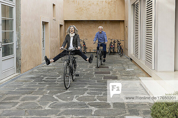 Happy senior woman riding bicycle with man on footpath