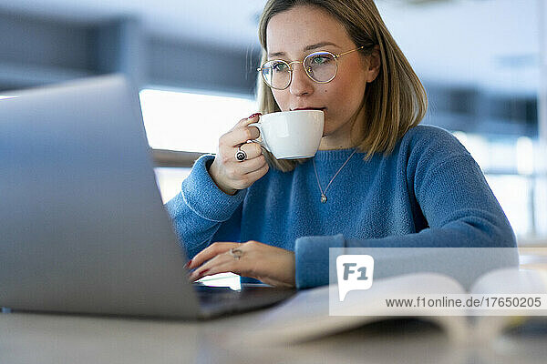 Young woman drinking coffee and using laptop at table
