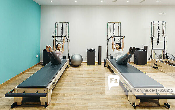 Woman with fitness instructor practicing stretching exercise on reformer