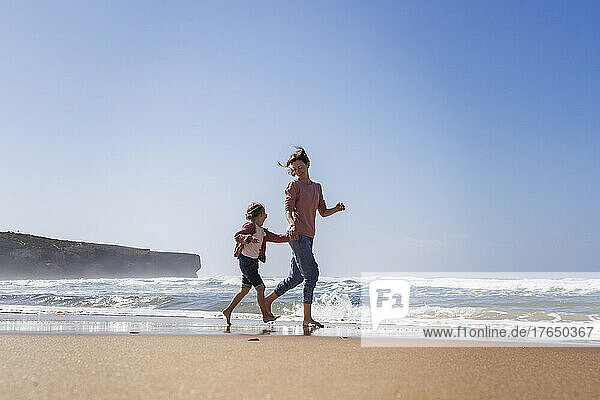 Happy mother and daughter running at beach on sunny day