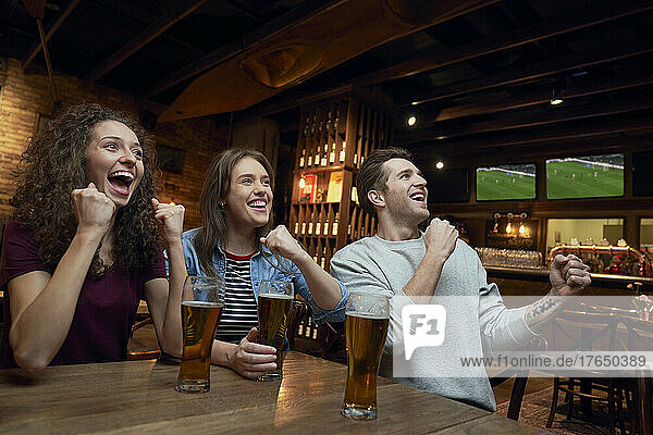 Cheerful soccer fans having beer and watching a match together in a pub