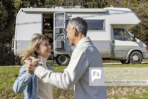 Happy mature couple holding hands by motor home on vacation