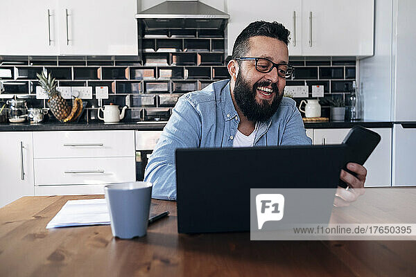 Happy freelancer with laptop using smart phone at home
