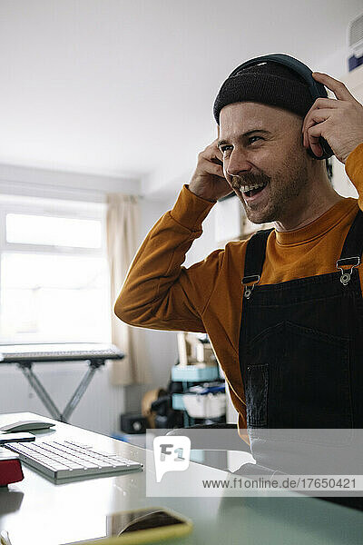 Happy freelancer wearing headphones sitting at table in home studio