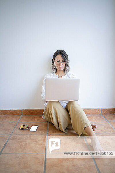 Young freelancer using laptop sitting in front of wall