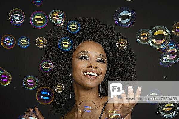 Smiling young woman amidst soap bubbles against black background