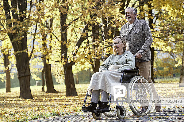 Senior man walking with disabled woman sitting in wheelchair at park