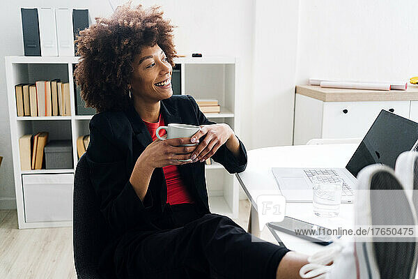 Smiling businesswoman sitting at desk with coffee cup in office