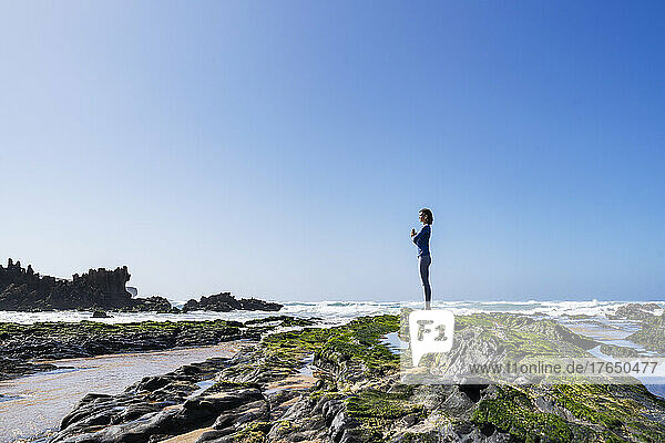 Frau mit gefalteten Händen steht auf einem Felsen am sonnigen Strand