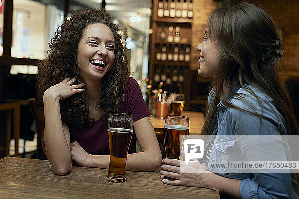 Zwei glückliche Freundinnen trinken Bier und unterhalten sich in einer Kneipe