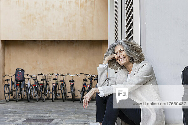Happy senior woman with gray hair sitting in front of wall