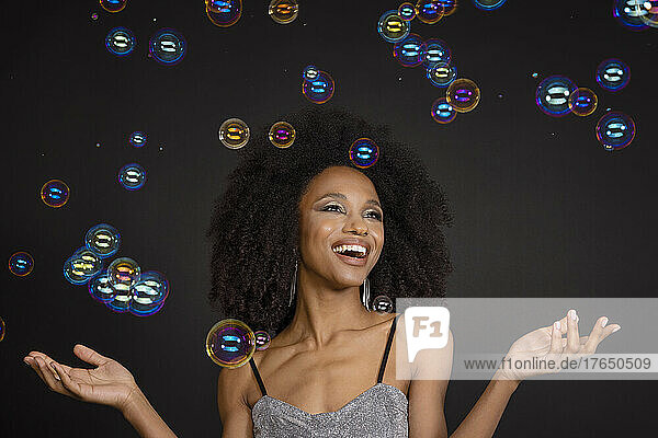 Glückliche junge Frau  die Seifenblasen vor schwarzem Hintergrund betrachtet