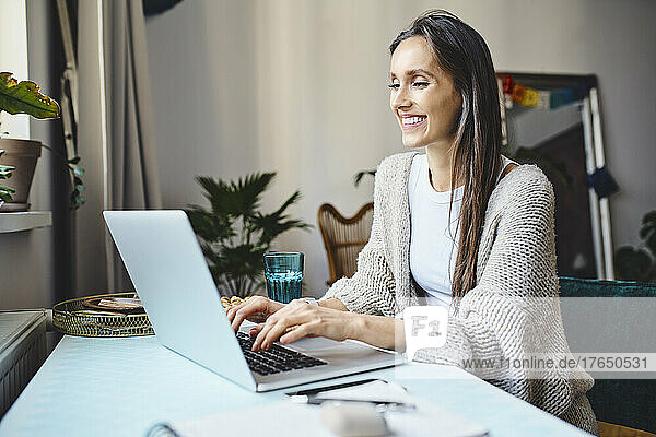 Happy freelancer with long hair working on laptop at home