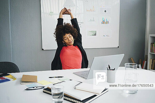Tired young businesswoman stretching at desk in office