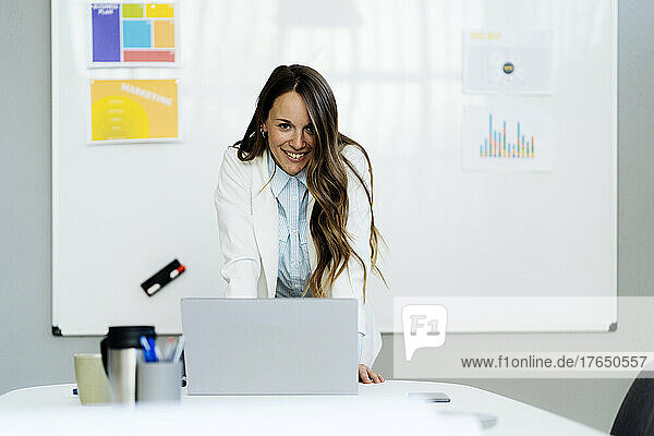 Happy businesswoman with laptop at desk in office