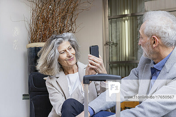 Smiling senior woman photographing man through mobile phone