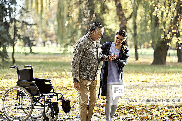 Healthcare worker helping senior disabled man walking at park