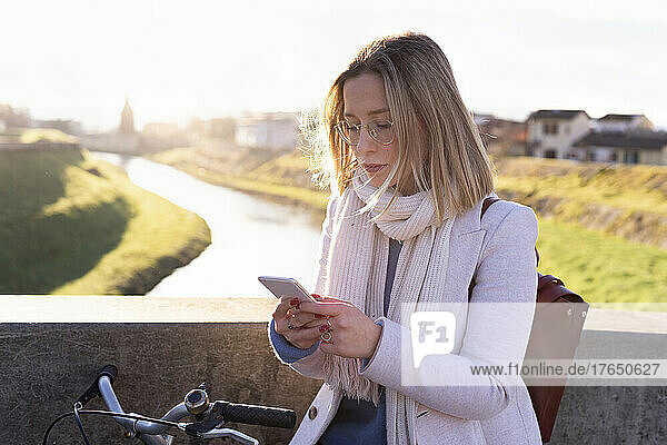 Young woman with bicycle using mobile phone on sunny day