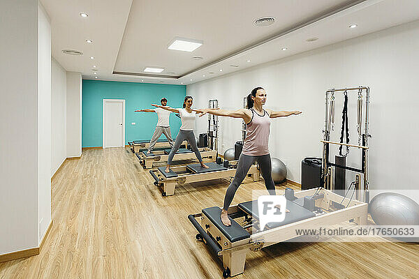 Man and women with arms outstretched exercising on reformer equipment in studio
