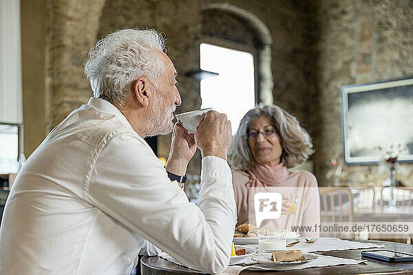 Smiling senior couple drinking coffee sitting with woman at table in boutique hotel
