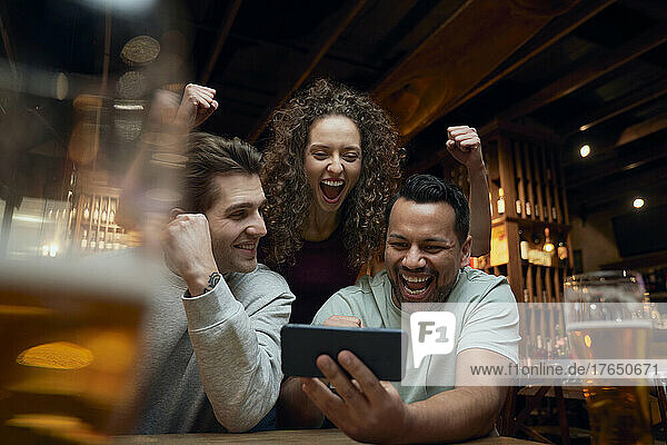 Fröhliche Fußballfans trinken Bier und schauen sich ein Spiel auf dem Smartphone in einer Kneipe an