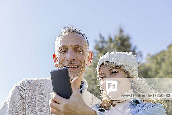 Smiling mature couple taking selfie over smart phone on sunny day
