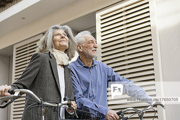 Glückliches älteres Paar  das mit Fahrrädern vor dem Gebäude steht