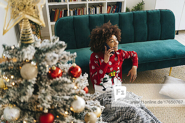 Smiling woman talking on mobile phone leaning on sofa at home