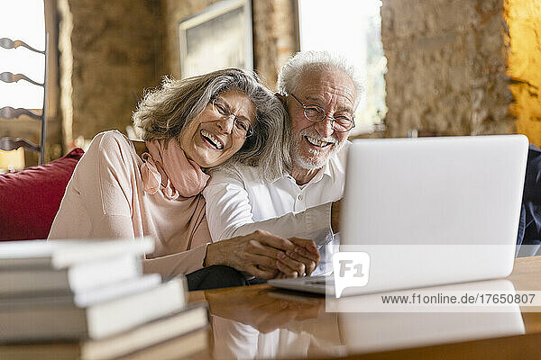 Happy senior couple sharing laptop sitting on sofa in boutique hotel