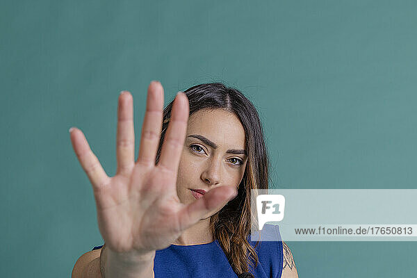 Young woman gesturing stop with hand against blue background