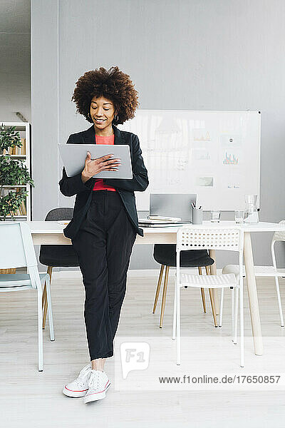 Afro businesswoman leaning on desk and using tablet PC in office