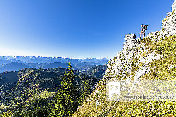 Männlicher Wanderer bewundert die bewaldete Landschaft der Bayerischen Voralpen vom Rand eines steilen Bergrückens aus