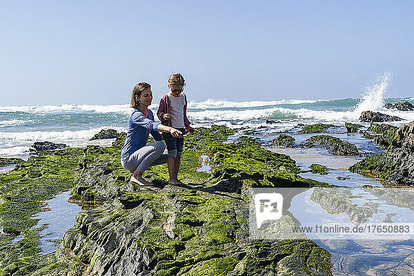 Mutter zeigt an sonnigem Tag auf Tochter am felsigen Strand