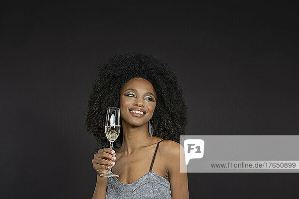 Smiling young woman holding champagne flute against black background