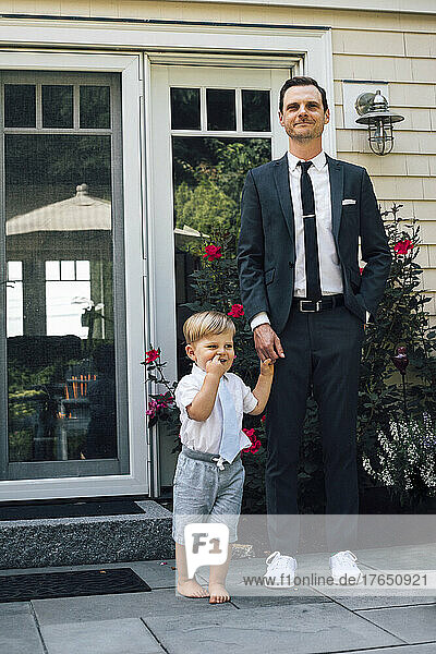 Father and son holding hands standing in front of house door