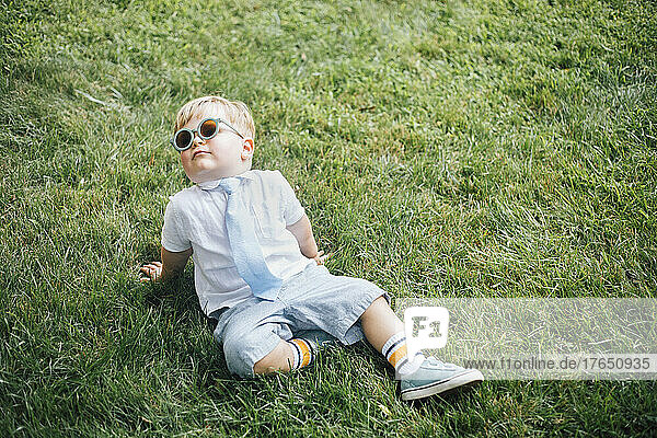 Boy wearing sunglasses and necktie sitting on grass