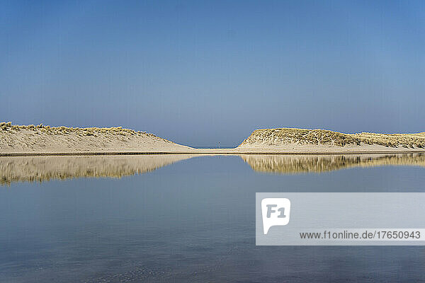 Lagune mit Sanddünen unter klarem Himmel