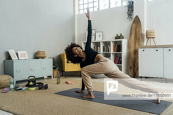 Smiling young woman with hand raised exercising in living room at home