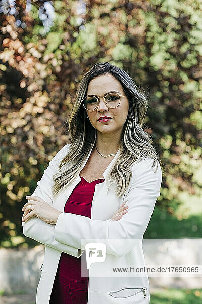 Confident businesswoman standing with arms crossed at park