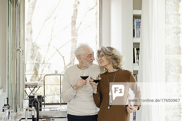 Happy senior couple with wineglasses standing in hotel apartment