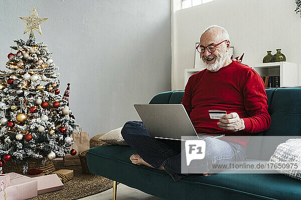 Happy senior man holding credit card doing online shopping sitting on sofa at home