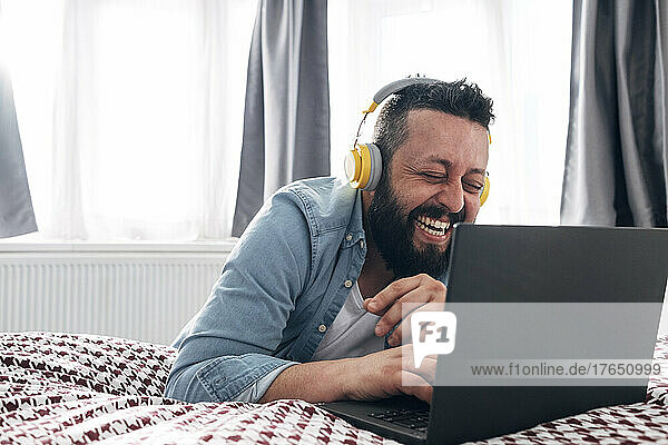 Glücklicher Mann mit kabellosen Kopfhörern  der zu Hause einen Laptop benutzt