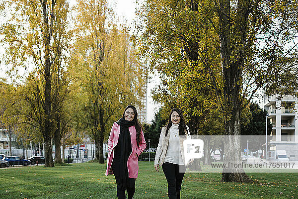 Happy sisters walking in front of trees at public park